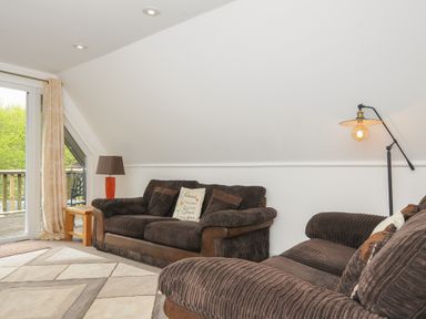 A living room with brown sofas a floor lamp and a wooden side table near a glass door at Valley Lodge 55 Callington near Gunnislake