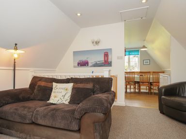A living area with a brown sofa and armchair a dining table with chairs in the adjacent room at Valley Lodge 55 Callington near Gunnislake