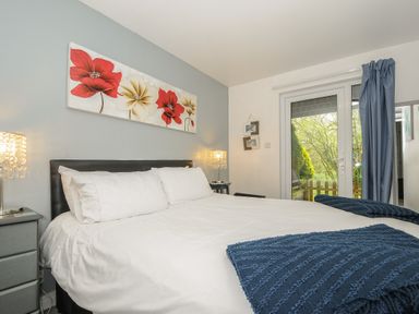 A bedroom with a double bed white bedding blue throws bedside tables with lamps and a glass door with blue curtains at Valley Lodge 55 Callington near Gunnislake