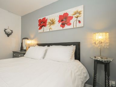 A bedroom with a bed white bedding a bedside table with a lamp and a painting of red and beige flowers on the wall at Valley Lodge 55 in Callington near Gunnislake
