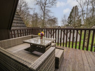 A balcony with a wicker seating set and glass table with flowers overlooking a grassy area at Valley Lodge 33 Callington near Gunnislake