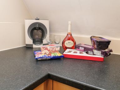 A kitchen counter with a coffee machine two glasses a bottle of Mateus rose wine sweets and chocolate at Valley Lodge 33 Callington near Gunnislake