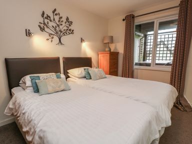 A bedroom with two single beds a wooden chest of drawers a table lamp and a window with curtains at Valley Lodge 33 Callington near Gunnislake