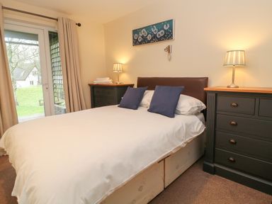 A bedroom with a double bed two blue pillows two black dressers with lamps and curtains at Valley Lodge 33 Callington near Gunnislake