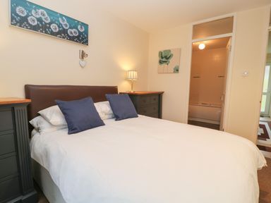 A bedroom with a bed with blue pillows two bedside dressers and a doorway leading to a bathroom at Valley Lodge 33 Callington near Gunnislake