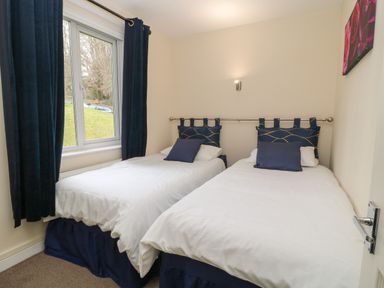 A bedroom with two single beds with white bedding and blue headboards and curtains at Valley Lodge 33 in Callington near Gunnislake