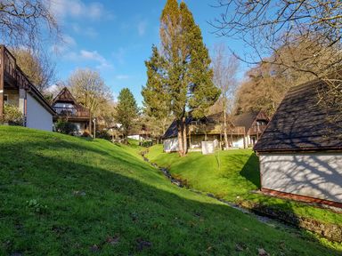 A row of holiday lodges with pitched roofs along a stream in a grassy area with trees at Valley Lodge 33 Callington near Gunnislake