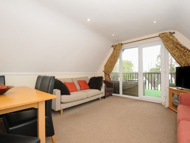 A living room with a beige sofa and red cushions near glass doors with yellow curtains at Valley Lodge 33 in Callington near Gunnislake