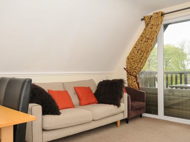 A living room with a beige sofa with red and dark brown cushions next to a sliding glass door with yellow patterned curtains at Valley Lodge 33 in Callington near Gunnislake