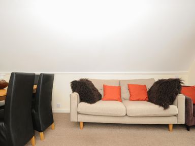 A beige sofa with red and dark brown pillows next to black dining chairs on a carpeted floor at Valley Lodge 33 in Callington near Gunnislake