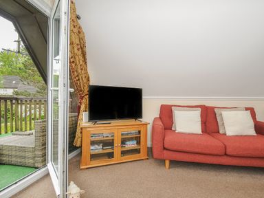A corner of a living room with a red sofa and a television on a wooden cabinet near an open glass door leading to a balcony at Valley Lodge 33 Callington near Gunnislake
