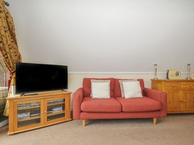 A living room with a red sofa two cushions a wooden TV stand with a television and a wooden cabinet with decorative items at Valley Lodge 33 Callington near Gunnislake