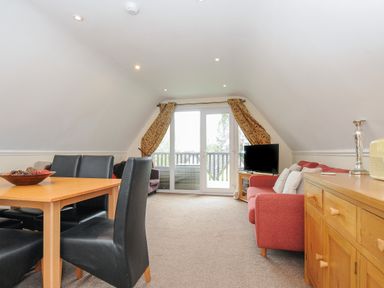 A living room with a dining table and black chairs a red sofa a wooden sideboard and a television at Valley Lodge 33 in Callington near Gunnislake