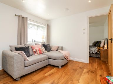 A living room with a gray sectional sofa and cushions by a window with beige curtains at Cosy Cottage in Broadwoodwidger near Lifton