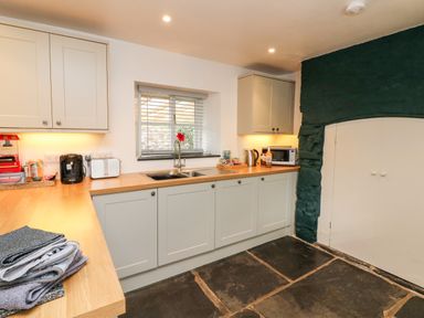 A kitchen with cream cabinets a wooden countertop a window above a double sink and a dark stone floor at Cosy Cottage Broadwoodwidger near Lifton