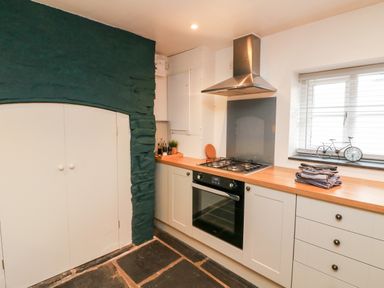 A kitchen with a gas stove oven wooden countertop white cabinets and a window with blinds at Cosy Cottage in Broadwoodwidger near Lifton