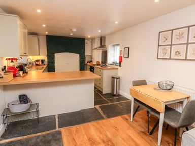 A kitchen with wooden countertops a dining table with two chairs and framed botanical prints on the wall at Cosy Cottage in Broadwoodwidger near Lifton