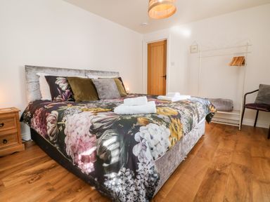 A bedroom with a floral bedspread wooden floor a wooden door a bedside table and a clothing rack at Cosy Cottage Broadwoodwidger near Lifton