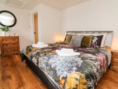 A bedroom with a floral bedspread and wooden furniture at Cosy Cottage in Broadwoodwidger near Lifton