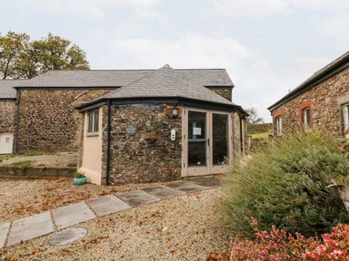 A stone building with a tiled roof and glass doors next to gravel path and shrubs at Cosy Cottage in Broadwoodwidger near Lifton