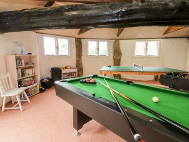 A games room with a pool table ping pong table foosball table books on shelves and a white chair at Cosy Cottage in Broadwoodwidger near Lifton