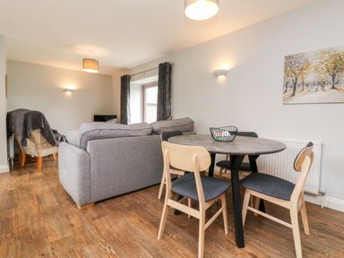A living room with a dining table and chairs and a sofa at The Old Cowshed in Broadwoodwidger near Lifton