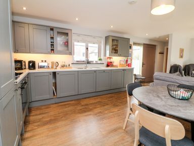 A kitchen with gray cabinets wooden floor and a round dining table with chairs at The Old Cowshed in Broadwoodwidger near Lifton