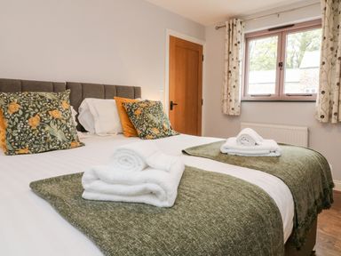 A bedroom with two single beds and floral curtains at The Old Cowshed Broadwoodwidger near Lifton