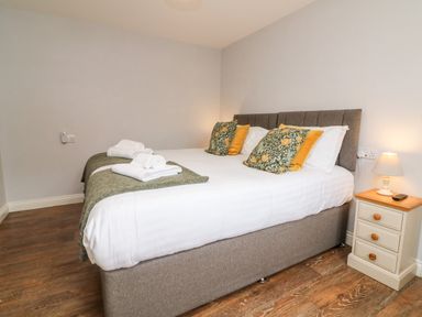 A bedroom with a bed with pillows and folded towels on it and a bedside table with a lamp at The Old Cowshed in Broadwoodwidger near Lifton