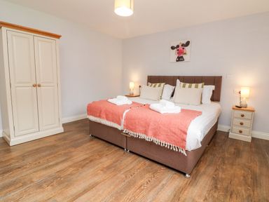 A bedroom with a double bed with pillows and blankets two bedside tables with lamps and a wardrobe at The Old Cowshed Broadwoodwidger near Lifton
