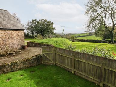 A garden with lawn chairs patio and wooden fence overlooking a green field at The Old Cowshed in Broadwoodwidger near Lifton