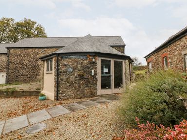 An octagonal stone building with glass double doors and a slate roof with a garden path leading to it at The Old Cowshed in Broadwoodwidger near Lifton
