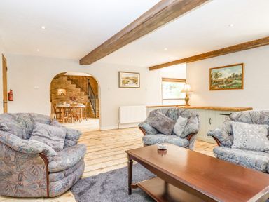 A living room with patterned sofas wooden coffee table and a dining area visible through an archway at Bunts Barn in Northlew near Hatherleigh