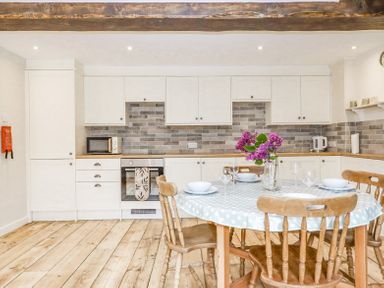 A kitchen with white cabinets wooden table and chairs with a polka dot tablecloth and flowers at Bunts Barn Northlew near Hatherleigh
