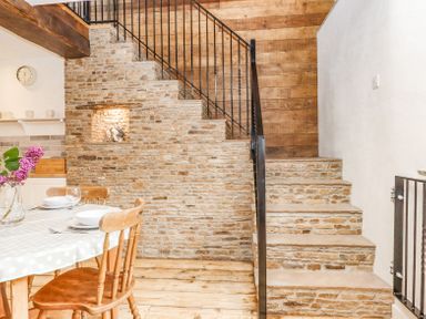 A dining area with a wooden table and chairs next to stone stairs with a metal railing at Bunts Barn Northlew near Hatherleigh