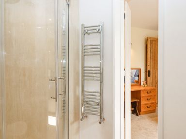 A bathroom with a glass shower door and a chrome towel rack visible through an open door into a bedroom with a wooden dresser and a wardrobe at Bunts Barn Northlew near Hatherleigh