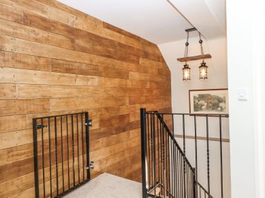 A staircase with black metal railings and a wooden paneled wall with two hanging lights and a framed picture at Bunts Barn in Northlew near Hatherleigh