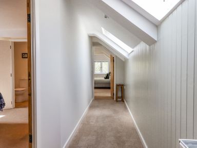 A narrow hallway with beige carpet and a wooden stool under skylight windows at Bunts Barn Northlew near Hatherleigh