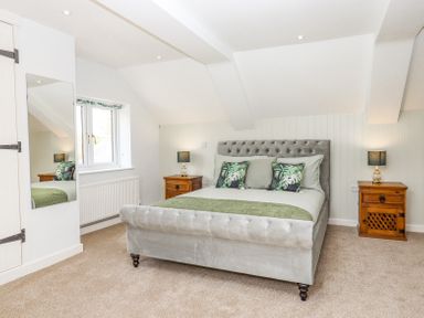 A bedroom with a grey upholstered bed with green pillows and two wooden bedside tables with lamps at Bunts Barn Northlew near Hatherleigh