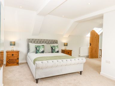 A bedroom with a bed between two wooden bedside tables and a wooden door at Bunts Barn in Northlew near Hatherleigh