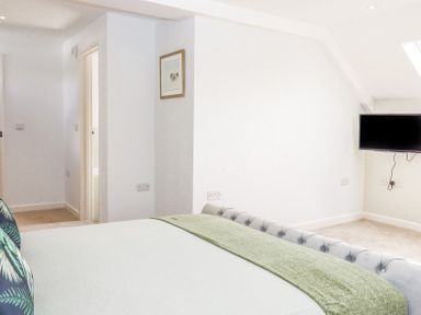 A bedroom with a bed a green blanket a wall-mounted television and a doorway at Bunts Barn in Northlew near Hatherleigh