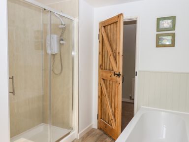 A bathroom with a glass shower enclosure a wooden door a bathtub and two framed pictures on the wall at Bunts Barn in Northlew near Hatherleigh