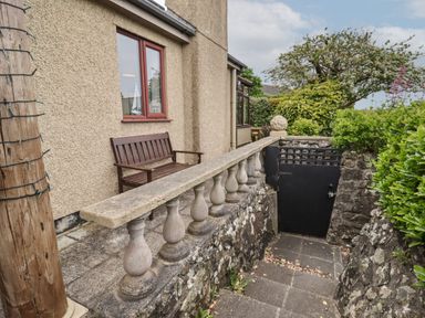 An outdoor area with a wooden bench stone balustrade stairs leading down to a black gate and surrounding vegetation at Spernenwyn in St Ives