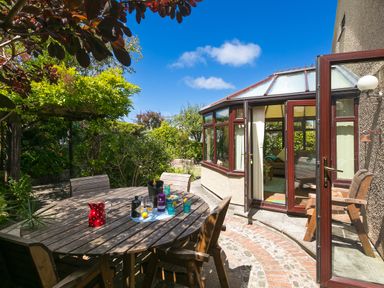 An outdoor dining area with wooden table and chairs next to a sunroom with glass doors at Spernenwyn St Ives