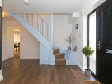 An entryway with wooden flooring a black front door light blue staircase and small potted plants at Spernenwyn in St Ives