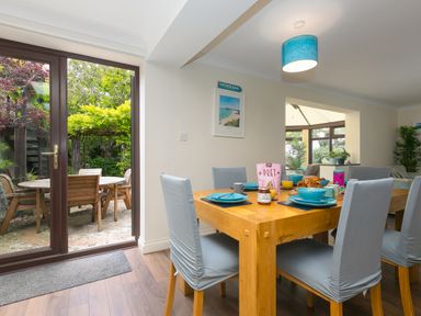 A dining area with a wooden table set for breakfast and chairs with light covers at Spernenwyn in St Ives