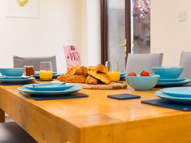 A dining table set with blue plates bowls glasses of orange juice croissants and strawberries at Spernenwyn in St Ives