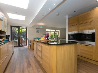 A kitchen with wooden cabinets a black countertop island double ovens and glass doors leading to a garden at Spernenwyn in St Ives