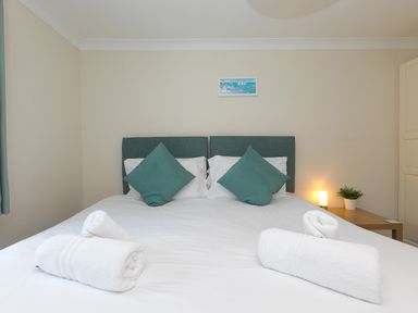 A bedroom with a double bed green pillows rolled white towels bedside table lamp and plant Spernenwyn St Ives