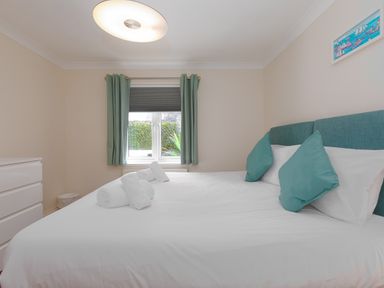 A bedroom with a large bed with teal pillows and white sheets a window with teal curtains and a white dresser at Spernenwyn in St Ives